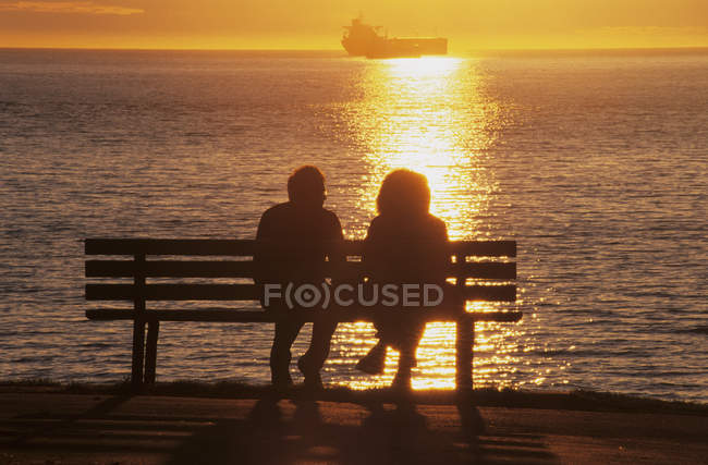 Silhuetas de casal no banco desfrutando do pôr do sol em Stanley Park, English Bay, Vancouver, British Columbia, Canadá — Fotografia de Stock