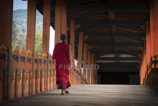 Visão traseira de monge adolescente andando através da ponte a caminho de Phunaka Dzong perto de Punakha, Butão . — Fotografia de Stock