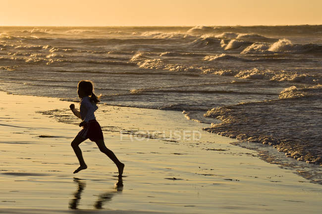 Chica preadolescente corriendo por la playa en Profitts Point cerca de Darnley, Prince Edward Island, Canadá . - foto de stock