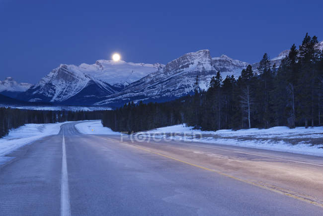 Autopista invernal y luna en el cielo en Bighorn Wildland, Alberta, Canadá - foto de stock