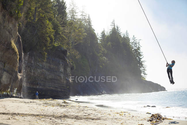 Jeune femme se balançant sur une corde à Mystic Beach le long du sentier Juan de Fuca, île de Vancouver, Canada — Photo de stock