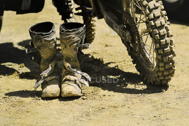 Dirty motocross boots and rear wheel of motocross bike — Stock Photo