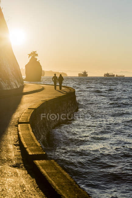 Silhouettes of couple strolling on Stanley Park seawall at sunset, Vancouver, British Columbia, Canada — Stock Photo