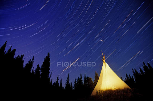 Senderos de estrellas sobre el tee-pee iluminado por la banda Canim Lake en las montañas Cariboo, Columbia Británica, Canadá . - foto de stock