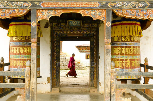 Joven monje que pasa por la puerta principal del monasterio butanés en Bután, Asia - foto de stock
