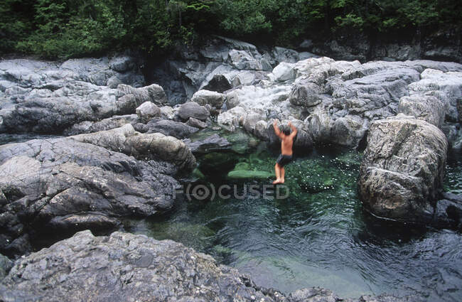 Река Кеннеди, на пути к Национальному парку Тихоокеанского региона, мальчик прыгает в чистую воду, остров Ванкувер, Британская Колумбия, Канада. — стоковое фото