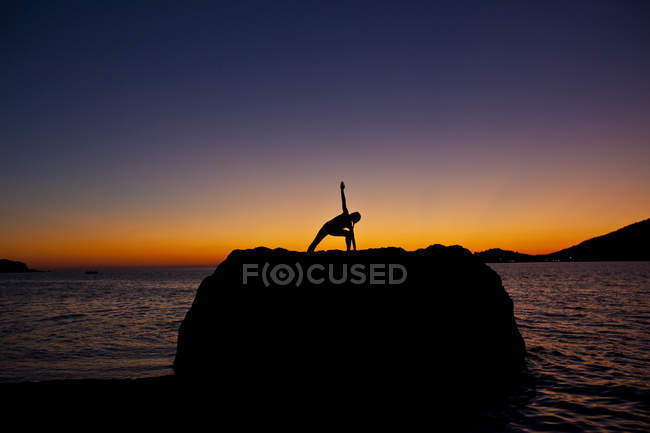 Silueta de mujer practicando yoga sobre roca costera al amanecer en Kalymnos, Grecia . - foto de stock