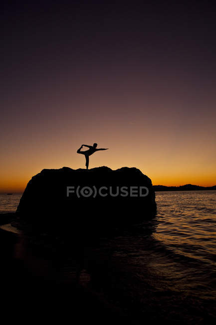 Silhouette di donna che pratica yoga sulla roccia costiera all'alba a Kalymnos, Grecia . — Foto stock