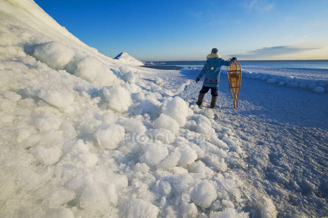 Un hombre con raquetas de nieve mira hacia fuera sobre pilas de hielo lavadas, a lo largo del lago Winnipeg, Manitoba, Canadá - foto de stock