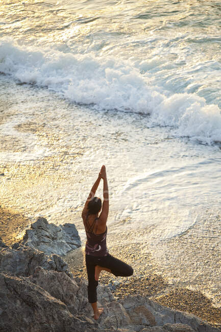 Високий кут зору жінки, яка робить йогу під час заходу сонця біля пляжу в Калімносі (Греція). — стокове фото