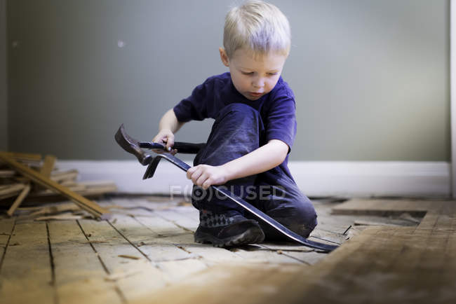 Menino pré-escolar jogando carpinteiro com pé de cabra, martelo e piso de madeira . — Fotografia de Stock