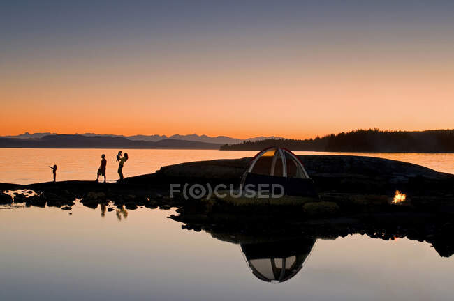 Una familia disfruta de una cautivadora puesta de sol mientras acampa cerca del río Powell, en la costa Sunshine de la costa de Vancouver y la región montañosa de Columbia Británica, Canadá. - foto de stock