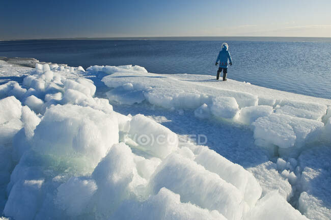 Un hombre mira hacia fuera sobre hielo que se derrite, a lo largo del lago Winnipeg, Manitoba, Canadá - foto de stock