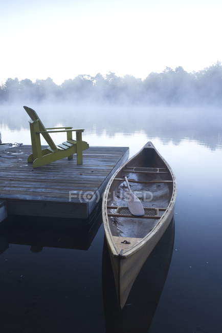 Moored wooden canoe at pier with patio chair on Muskoka lake in Ontario, Canada — Stock Photo