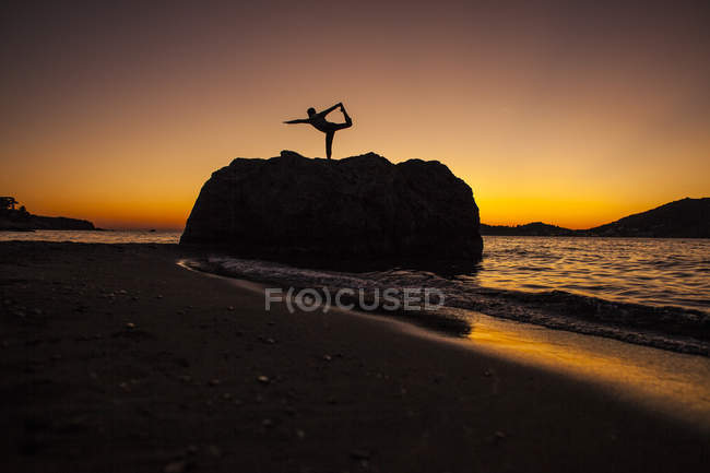 Silhueta de mulher praticando ioga na rocha costeira ao nascer do sol em Kalymnos, Grécia . — Fotografia de Stock