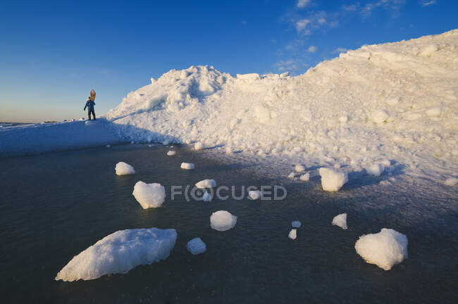 A man with snowshoes looks out over washed up ice piles, along Lake Winnipeg, Manitoba, Canada — Stock Photo