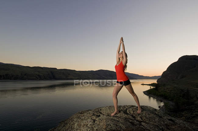 Mulher nova que pratica a arte do ioga sobre lago de Kamloops no por do sol, Kamloops, Colúmbia Britânica, Canadá — Fotografia de Stock