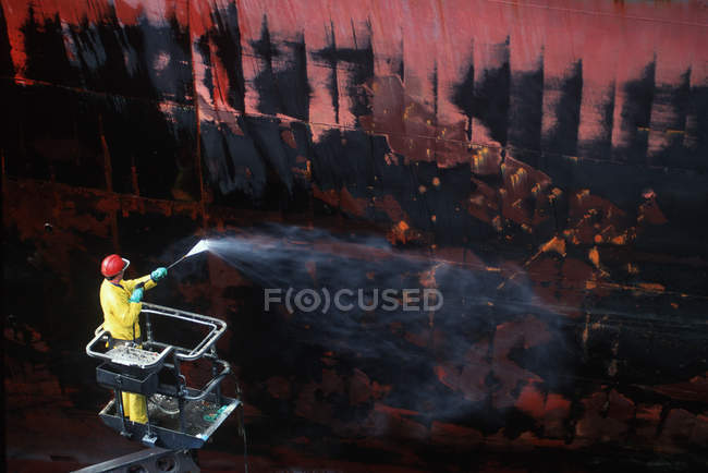 Shipyard worker powerwashing hull of steel ship, Victoria, Vancouver Island, British Columbia, Canada. — Stock Photo
