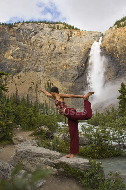 Jeune femme pratiquant le yoga sous les chutes Takakkaw dans le parc national Yoho, Colombie-Britannique, Canada — Photo de stock