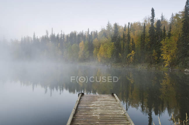 Molo di legno e fogliame autunnale di alberi forestali Dickens Lake, Saskatchewan settentrionale, Canada — Foto stock