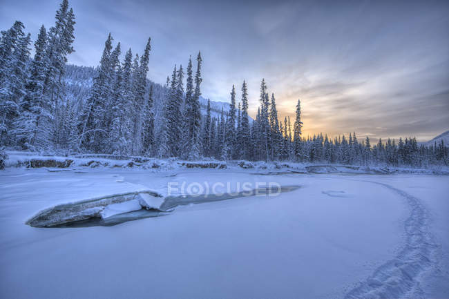 Pôr do sol no céu sobre o rio Wheaton congelado com trilhas a pé em Whitehorse, Yukon, Canadá . — Fotografia de Stock