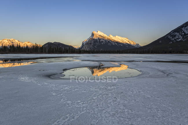 Mont Rundle reflétant dans la piscine sur le lac Vermilion gelé au coucher du soleil dans le parc national Banff, Alberta, Canada . — Photo de stock