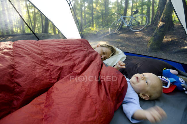 Молода мати з однорічним хлопчиком у наметі під час поїздки в кемпінг. Мама все ще намагається поспати. Rosebery Provincial Park, British Columbia — стокове фото