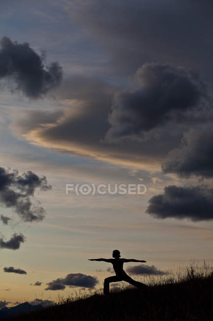 Silueta de mujer practicando yoga en la colina al amanecer en Canmore, Alberta, Canadá - foto de stock