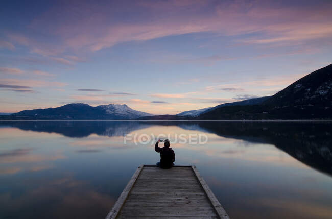Tirar uma fotografia enquanto aprecia as cores do pôr-do-sol sobre o Lago Shuswap, em Sunnybrae, perto de Salmon Arm, Colúmbia Britânica, Canadá. MR102 — Fotografia de Stock