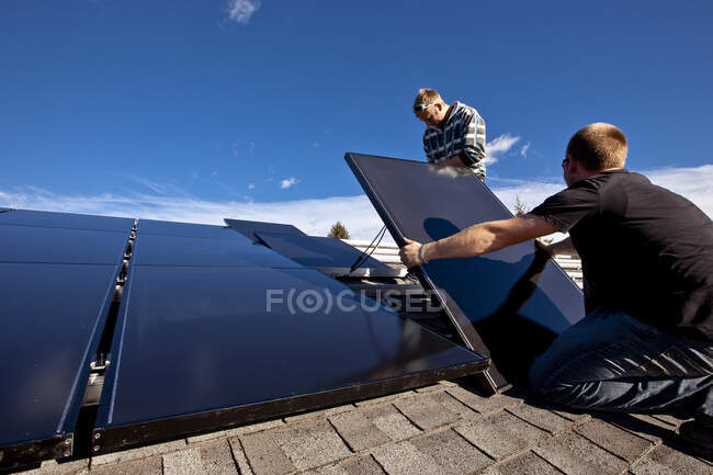 Два установщика солнечных батарей устанавливают солнечные батареи на крыше, предгорья Альберты возле Блэк Даймонд, Альберта, Канада. — стоковое фото