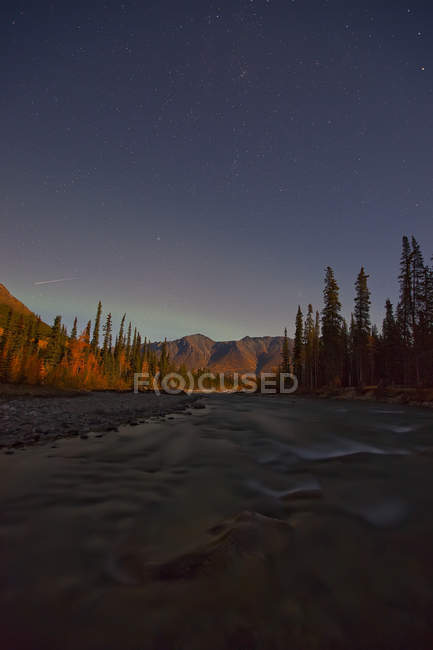 Rivière Wheaton la nuit avec ciel étoilé au-dessus des montagnes et aurore dans le ciel, Yukon, Canada . — Photo de stock