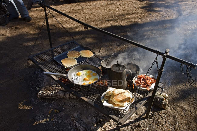 Fuego de campamento con sartenes llenas de comida para cocinar - foto de stock
