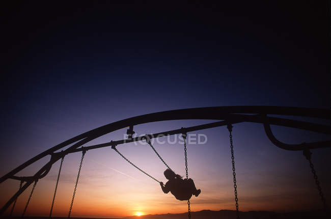 Criança em balanço em sillouette contra o céu do pôr do sol, Colúmbia Britânica, Canadá . — Fotografia de Stock