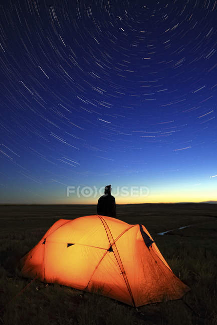 Pessoa olhando para as estrelas com tenda iluminada à noite com vista para o Vale do Rio Francês, Parque Nacional de Gramados, Saskatchewan . — Fotografia de Stock