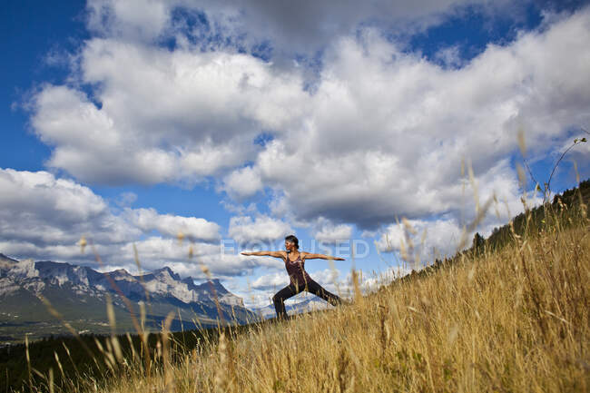 Товста жінка практикує позу воїна йоги на пагорбі за межами Канмора (Канада). — стокове фото