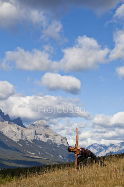 Fit woman practicing yoga triangle posture on hill in backcountry of Canmore, Canada — Stock Photo