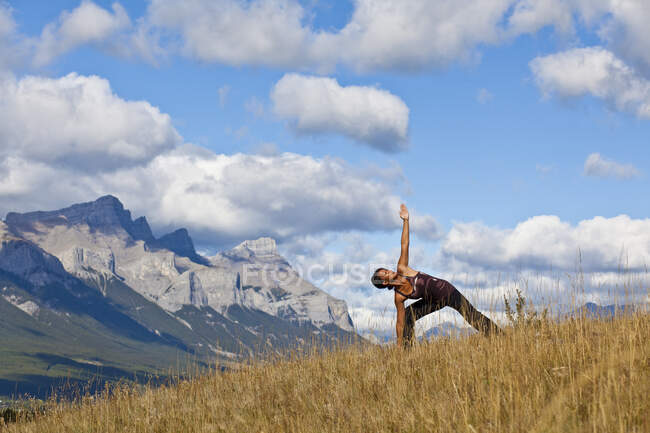 Fit woman practicing yoga triangle posture on hill in backcountry of Canmore, Canada — Stock Photo