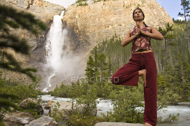 Jovem praticando ioga sob Takakkaw Falls no Parque Nacional Yoho, Colúmbia Britânica, Canadá — Fotografia de Stock