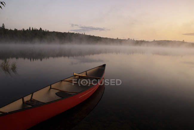 Canoa en la orilla con escena antes del amanecer del lago salvaje en el parque Algonquin, Ontario, Canadá - foto de stock
