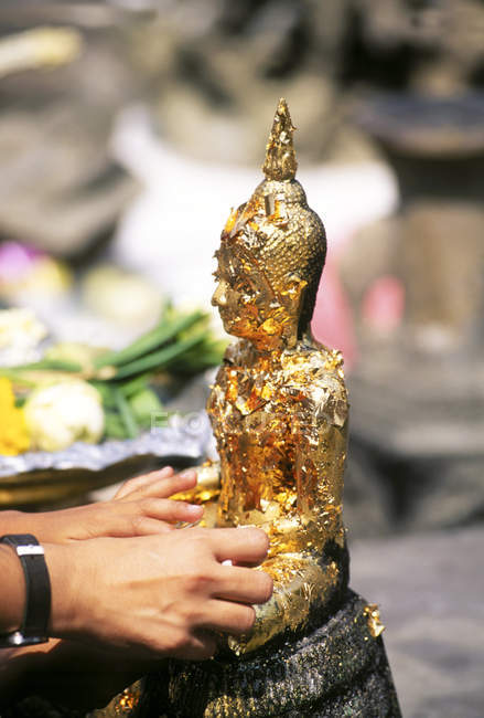 Manos femeninas aplicando hojas de oro a la estatua de Buda en el templo, Bangkok, Tailandia - foto de stock
