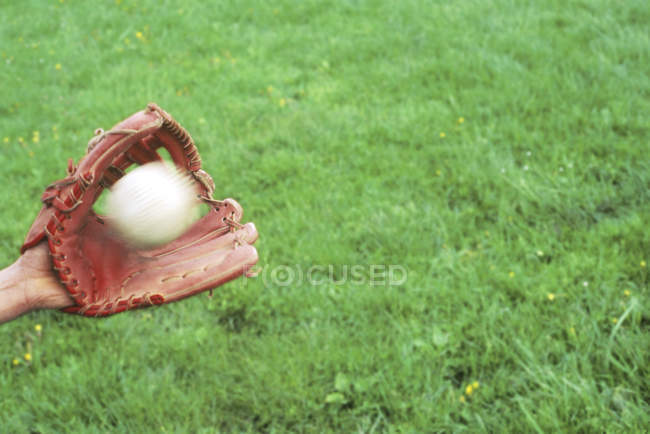 Luva para beisebol com bola voadora no fundo de grama verde — Fotografia de Stock