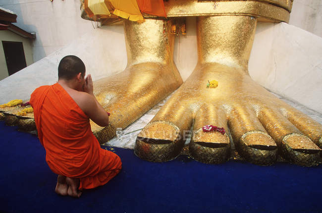 Monje haciendo ofrendas diarias a estatua de Buda en Wat Indrawahim, Bangkok, Tailandia - foto de stock