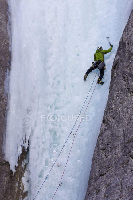 Homem escalador de gelo balançando machados em rocha face de montanhas de Ghost River, Alberta, Canadá — Fotografia de Stock
