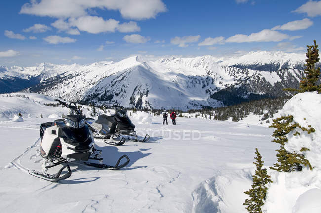 Amigos paran mientras motos de nieve, montañas Monashee, Valemount, Thompson Okanagan, Columbia Británica, Canadá - foto de stock