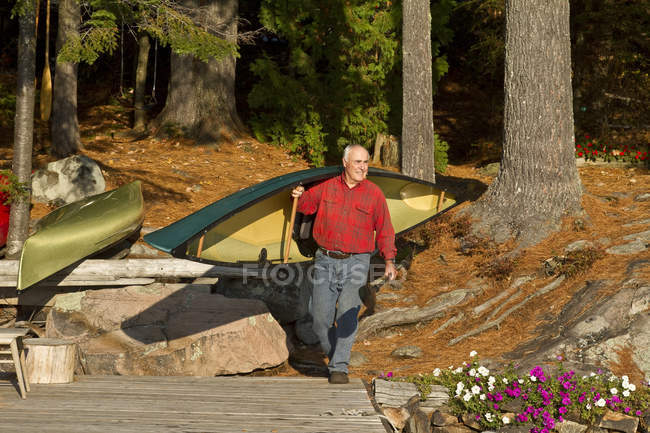Senior man carrying canoe onto dock at Muskoka, Ontario, Canada. — Stock Photo