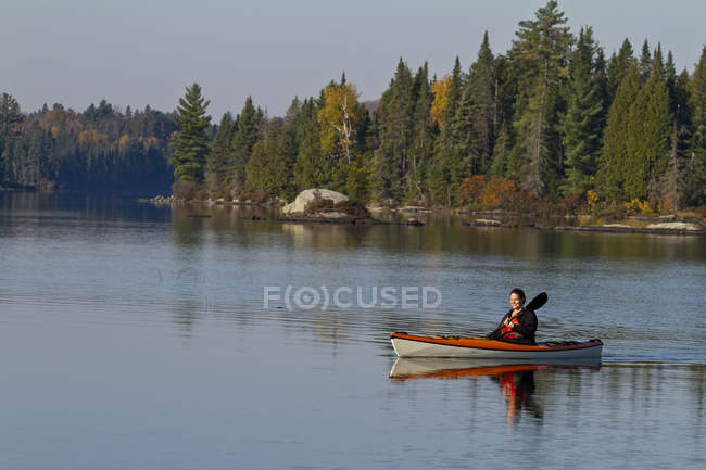 Donna che si gode la mattina in kayak sul lago sorgente, Algonquin Park, Ontario, Canada . — Foto stock