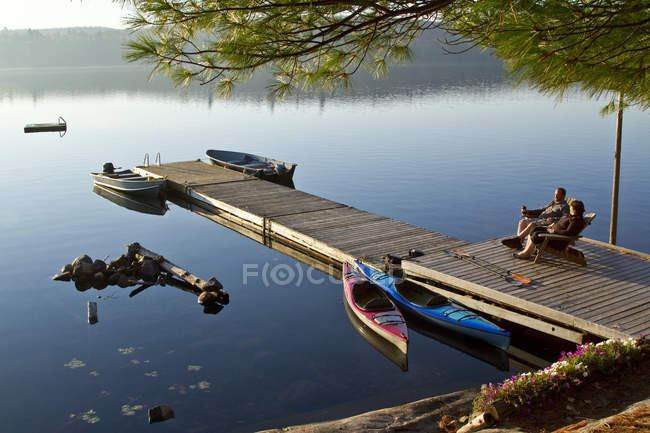 Middle-aged couple resting on dock of Source Lake, Algonquin Park, Ontario, Canada. — Stock Photo