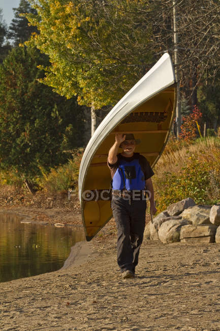 Mature man carrying canoe from water, Oxtongue Lake, Muskoka, Ontario, Canada. — Stock Photo