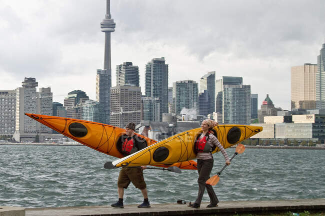 Parejas jóvenes llevan kayaks desde Lake Ontario, Toronto waterfront, Toronto, Ontario, Canadá. - foto de stock
