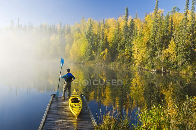 Человек, стоящий с веслом на причале с каяком, озеро Диккенс, Северный Саскачеван, Канада — стоковое фото